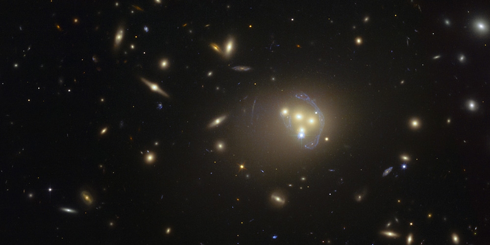 Deze foto, gemaakt met de Hubble-ruimtetelescoop van NASA en ESA, toont de rijke cluster van sterrenstelsels Abell 3827. De vreemde blauwe structuren rond de centrale sterrenstelsels zijn de vervormde afbeeldingen van een ver achtergrondstelsel, die ontstaan door het zwaartekrachtlenseffect.
