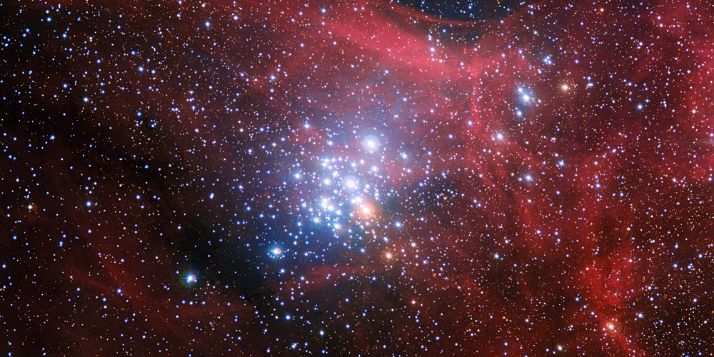 Op deze opname van de ESO-sterrenwacht op La Silla in Chili steekt een verzameling jonge sterren af tegen een achtergrond van wolken van gloeiend gas en banden van stof